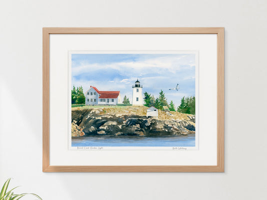 Framed watercolor print of Burnt Coat Harbor Light, Swans Island, in a warm wood frame on a neutral wall.