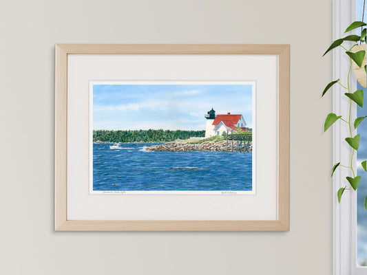 Framed watercolor print of Hendricks Head Light near Boothbay Harbor, in a warm wood frame beside a window.