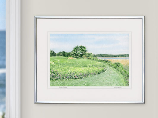 Framed watercolor print of North Meadow, Gilsland Farm, in a silver frame beside a window with an ocean view.