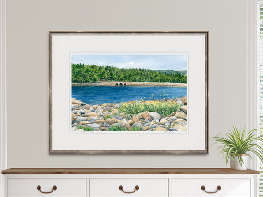 Framed watercolor print of Otter Cove Bridge, Acadia, Maine, in a warm wood frame on a dresser in a lifestyle setting.