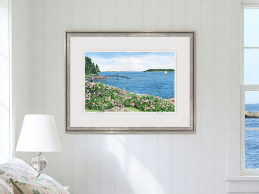 Framed watercolor print of Spruce Point, Boothbay Harbor, Maine, in a silver frame in a bedroom lifestyle setting.