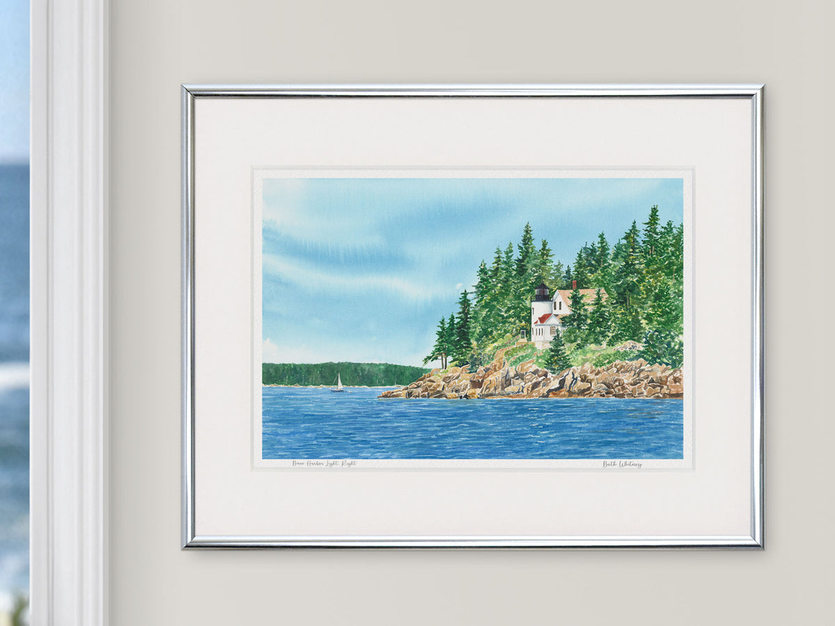 Framed watercolor print of Bass Harbor Light, Right, Acadia National Park, in a silver frame beside a window.