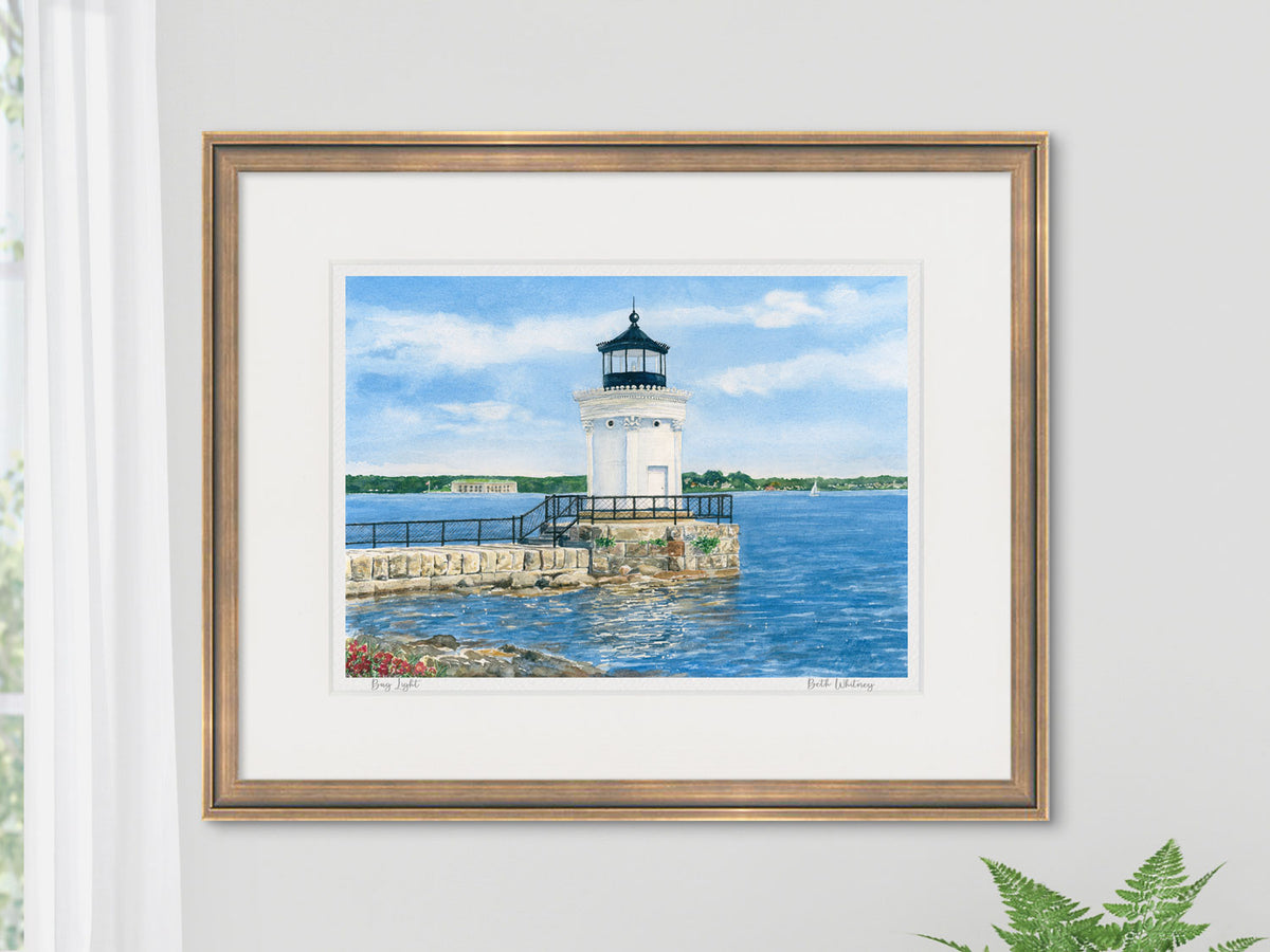 Framed watercolor print of Bug Light, South Portland, in a warm wood frame in an interior setting.
