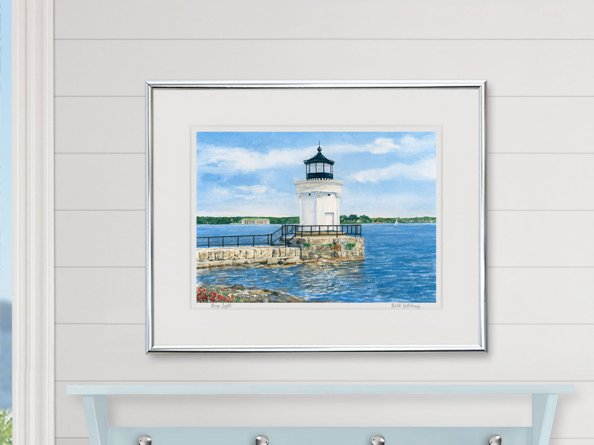 Framed watercolor print of Bug Light, South Portland, in a white frame in a bright lifestyle setting.