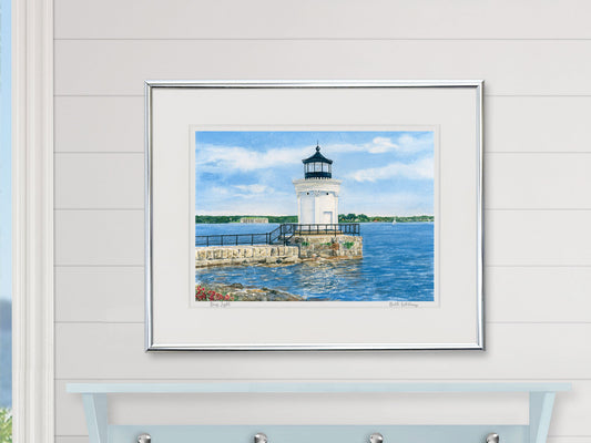 Framed watercolor print of Bug Light, South Portland, in a white frame in a bright lifestyle setting.