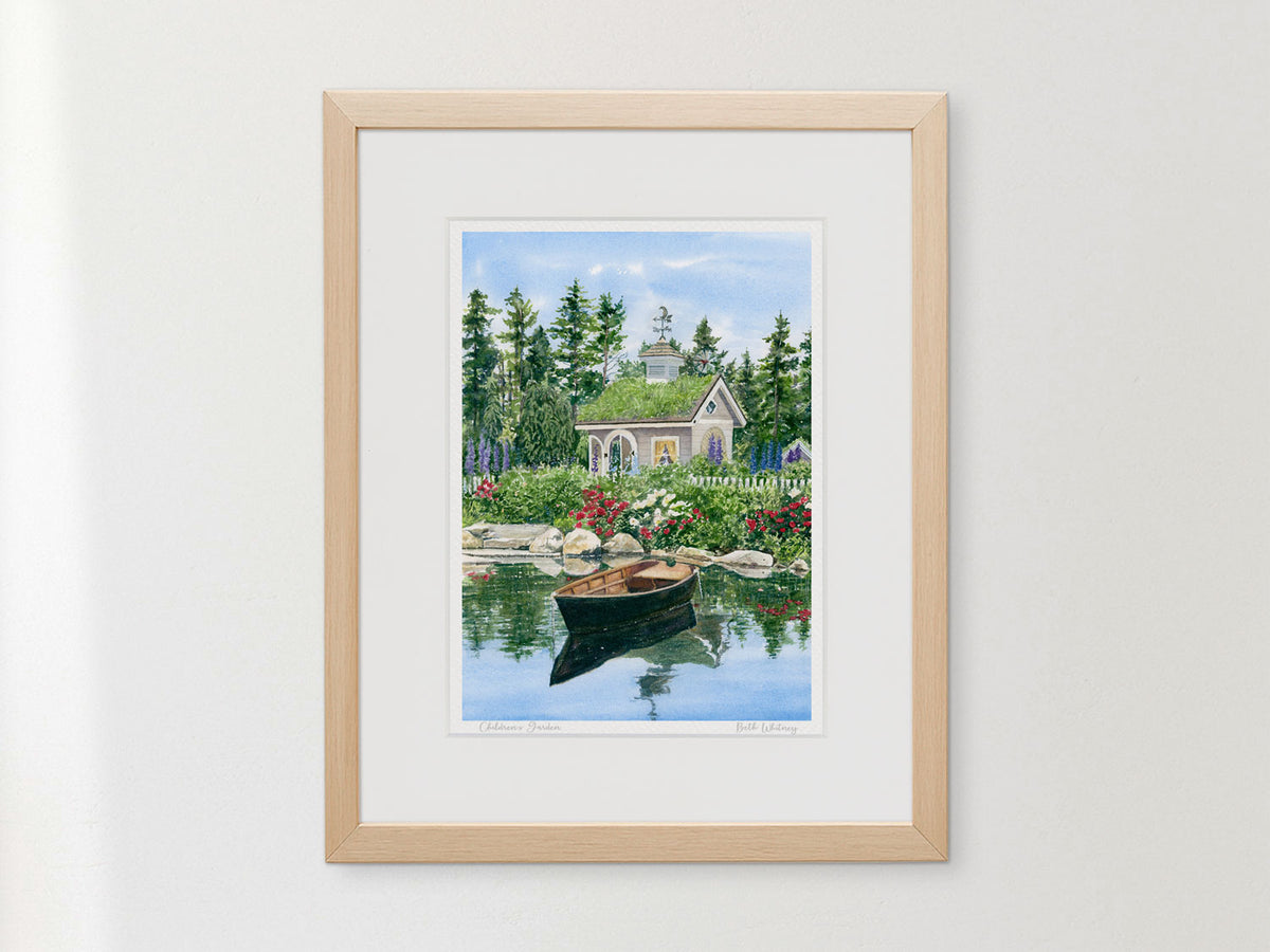 Framed watercolor print of Children's Garden, Coastal Maine Botanical Gardens, in a warm wood frame on a neutral wall.