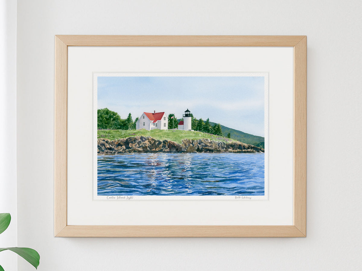 Framed watercolor print of Curtis Island Light, Camden, Maine, in a warm wood frame on a neutral wall.