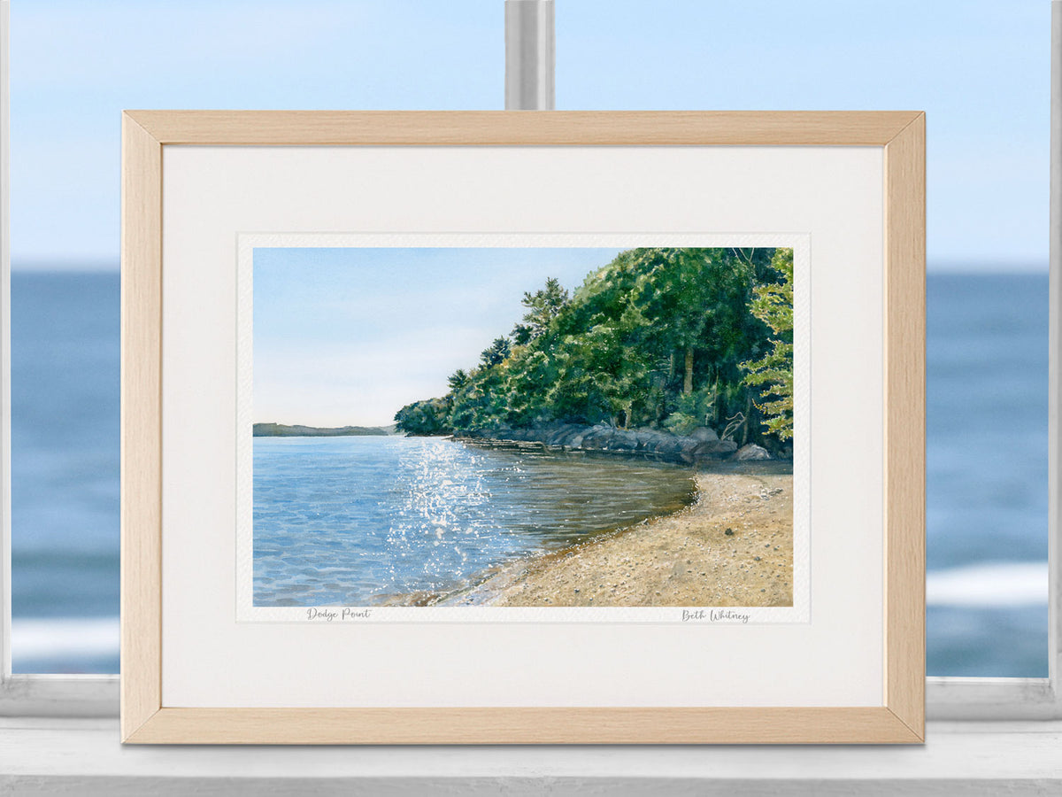 Framed watercolor print of Dodge Point, Damariscotta River, in a warm wood frame with natural window light.
