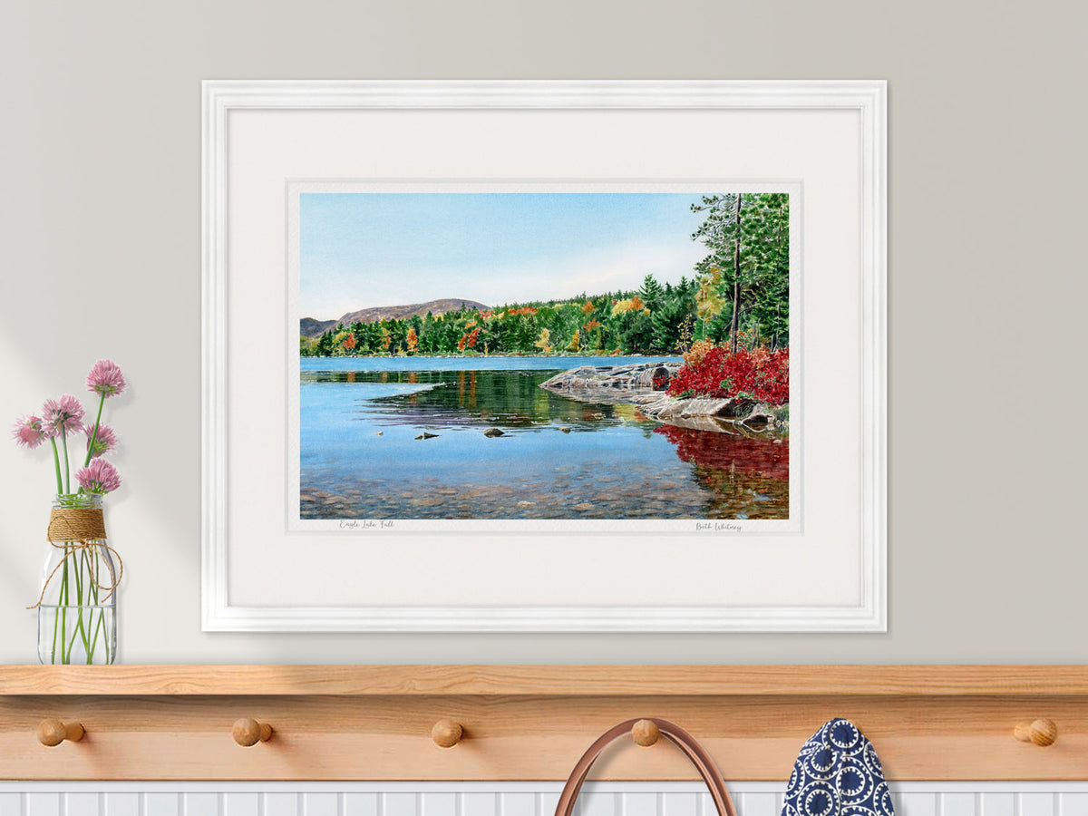 Framed watercolor print of Eagle Lake Fall, Acadia National Park, in a white frame over a wood coat rack.