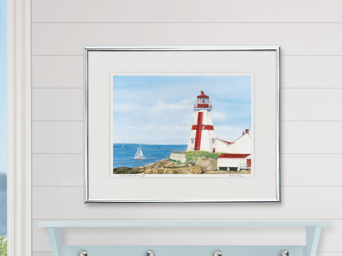 Framed watercolor print of East Quoddy Head Light in a silver frame on a shiplap wall.