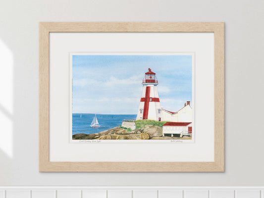 Framed watercolor print of East Quoddy Head Light in a natural wood frame on a light gray wall.
