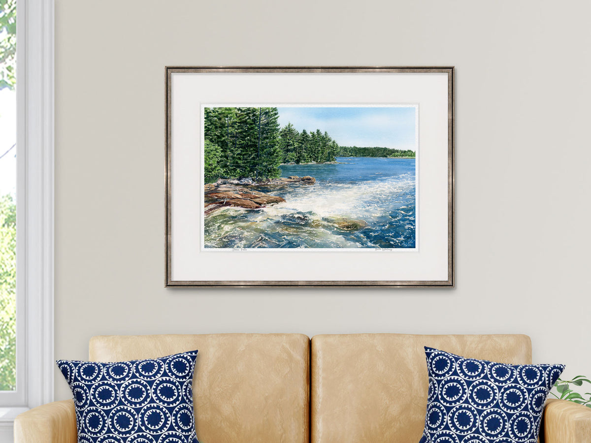 Framed watercolor print of Goose Falls, Harborside, Maine, in a copper frame above a sofa in a lifestyle setting.