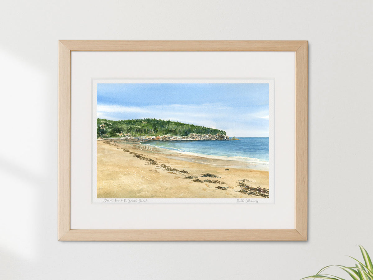 Framed watercolor print of Great Head and Sand Beach, Acadia National Park, in a warm wood frame on a neutral wall.