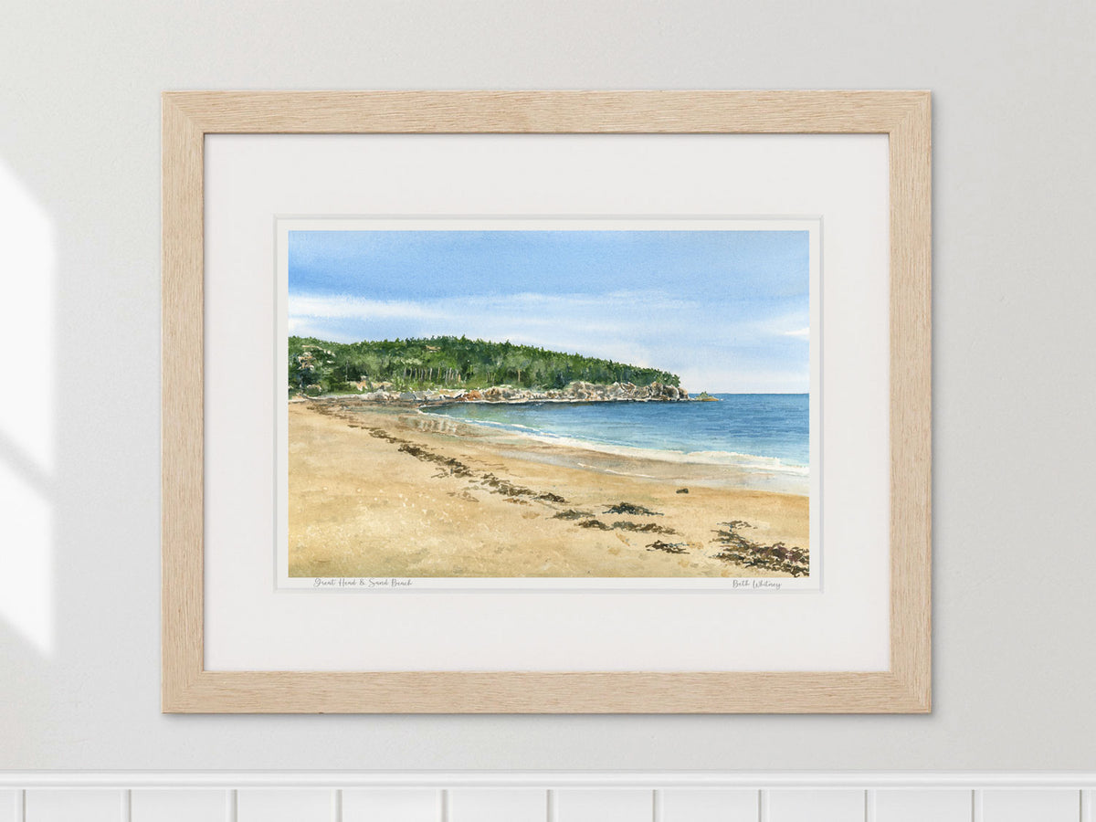 Framed watercolor print of Great Head and Sand Beach, Acadia, in a warm wood frame on a neutral wall.
