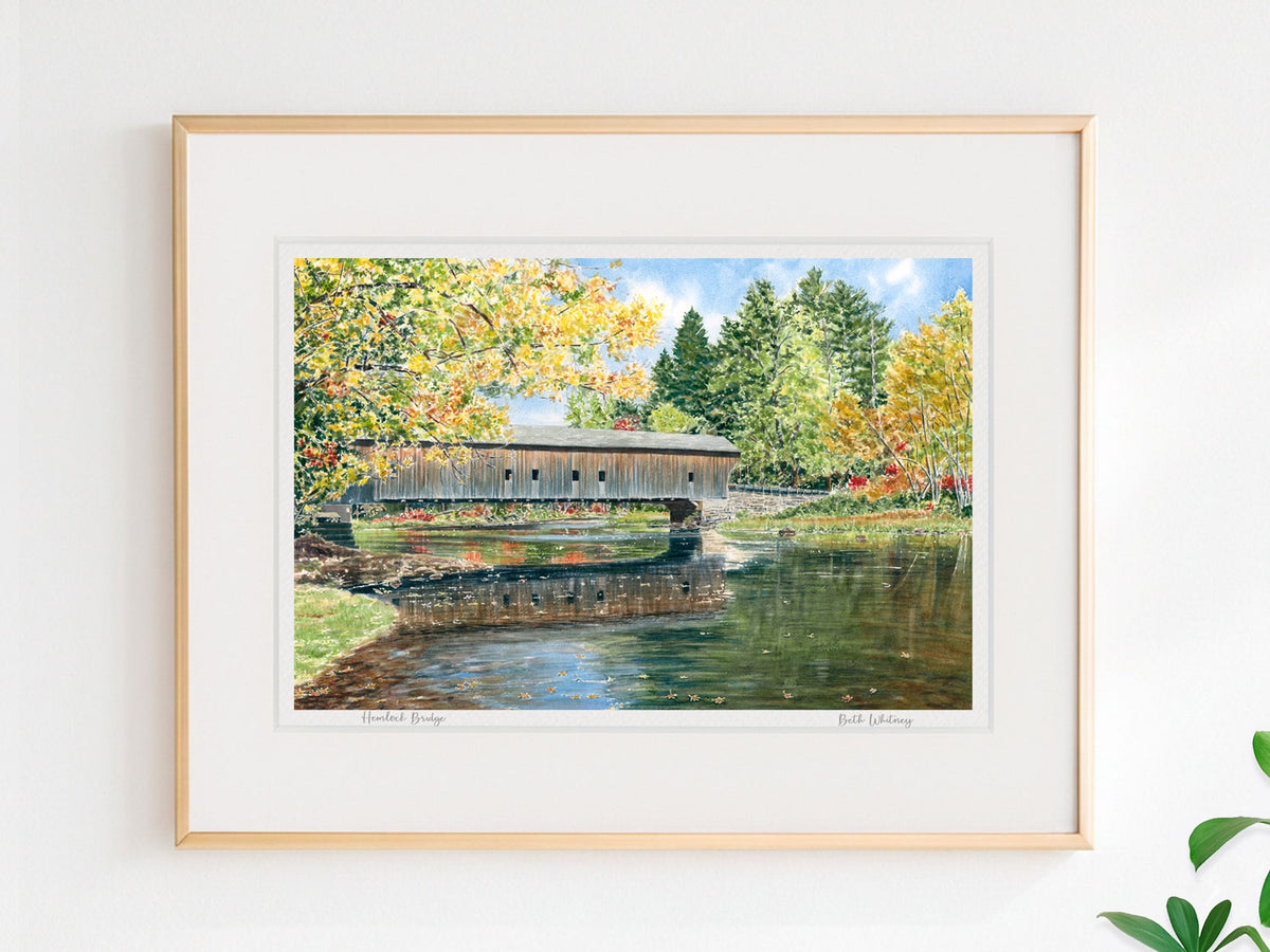 Framed watercolor print of Hemlock Bridge, Fryeburg, Maine, in a warm wood frame on a neutral wall.