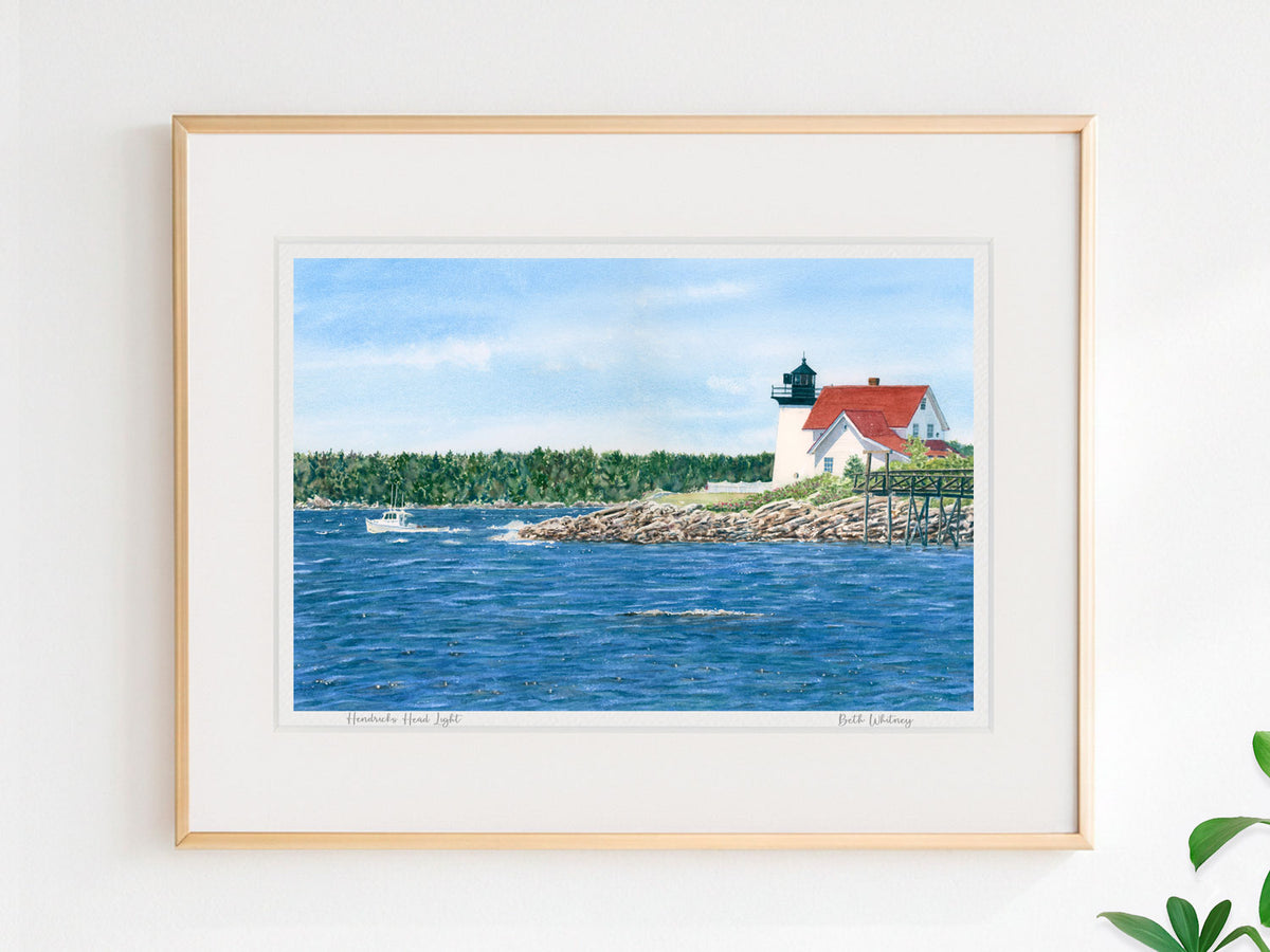 Framed watercolor print of Hendricks Head Light, Southport Island, in a warm wood frame on a neutral wall.