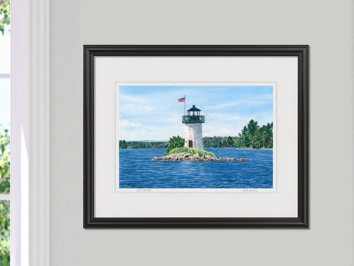 Framed watercolor print of Ladies Delight Light, Winthrop, Maine, in a black frame with natural window light.