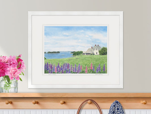 Framed watercolor print of Lupine Cottage, Deer Isle, in a white frame with peony styling over a coat rack.
