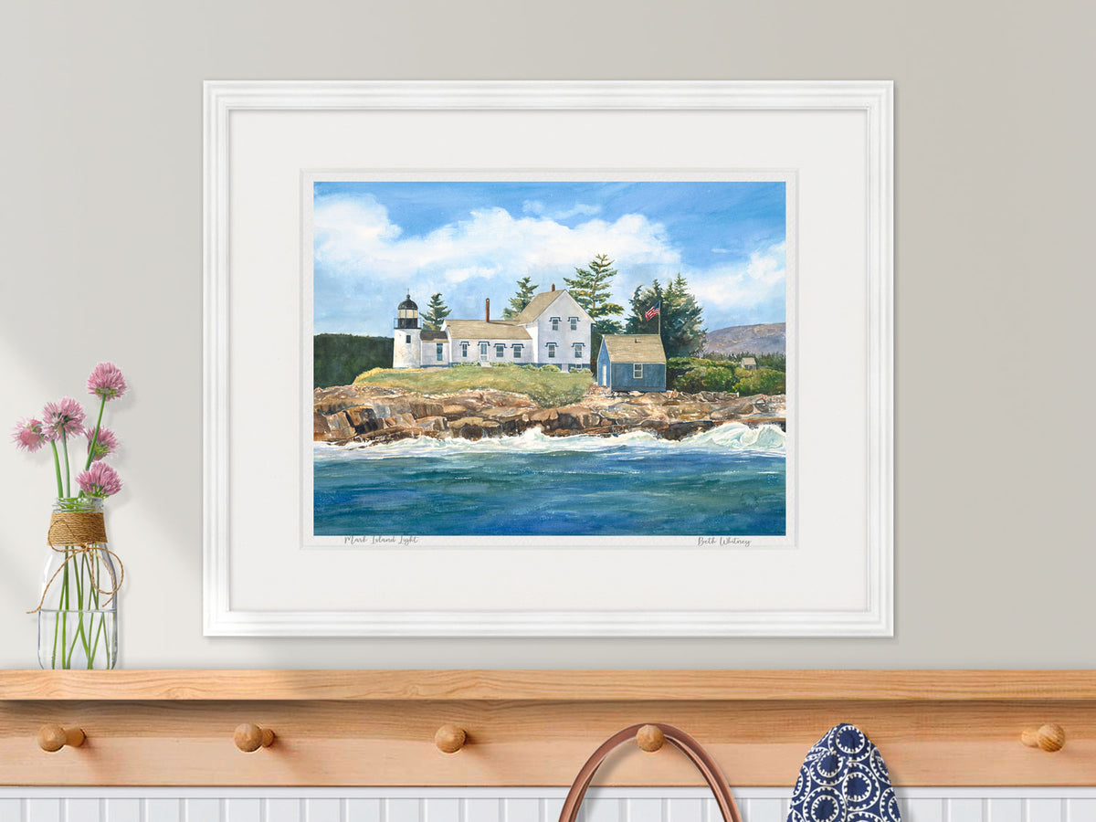 Framed watercolor print of Mark Island Light, Winter Harbor, in a white frame over a nautical coat rack.