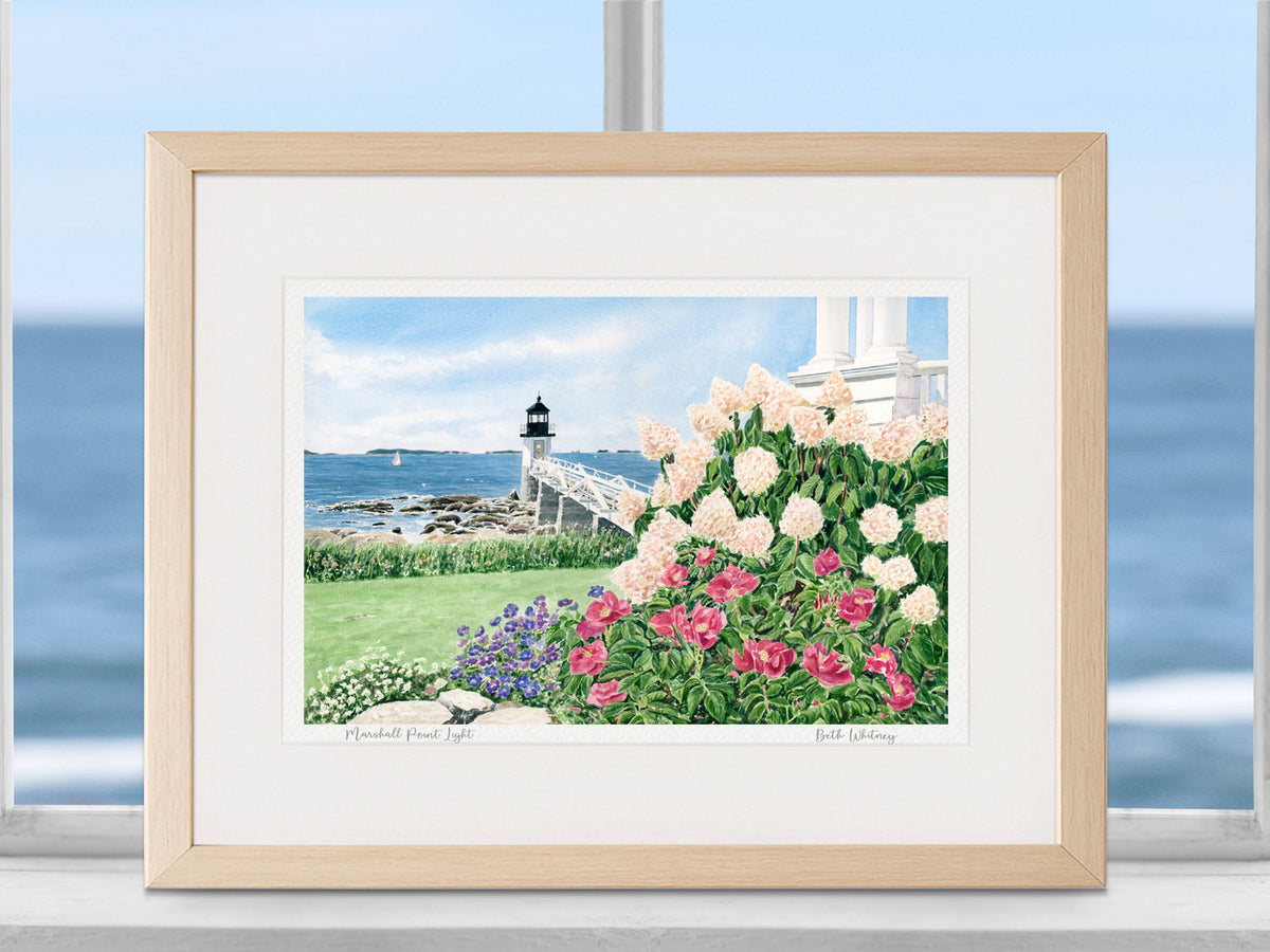 Framed watercolor print of Marshall Point Light, in a natural wood frame in a coastal window decor with the ocean beyond.