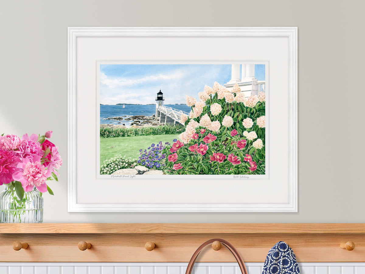 Framed watercolor print of Marshall Point Light, Maine, in a white frame with peony styling over a nautical wood coat rack.