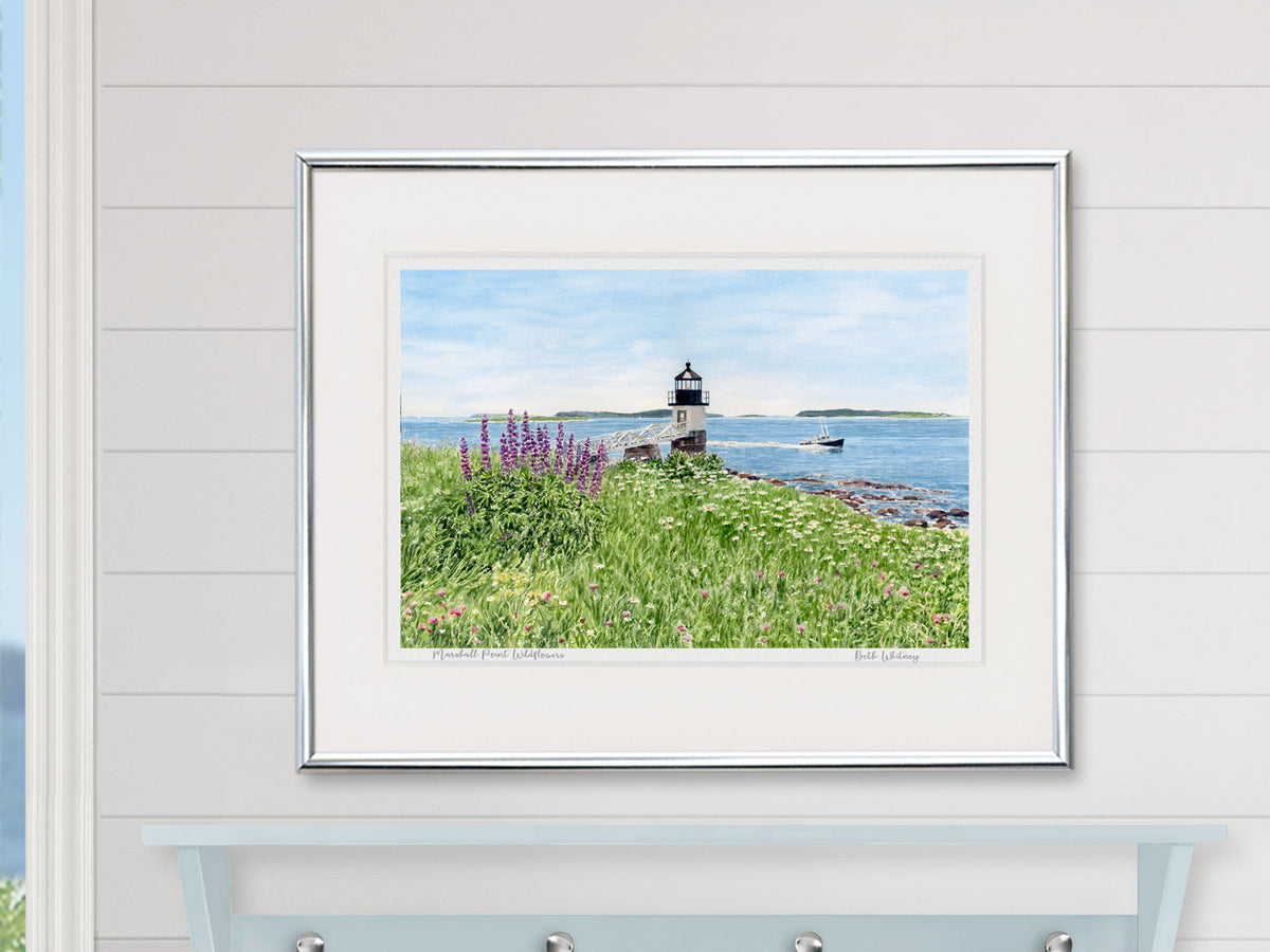 Framed watercolor print of Marshall Point Wildflowers, Tenants Harbor, in a silver frame on a shiplap wall over a pale blue shelf and window.