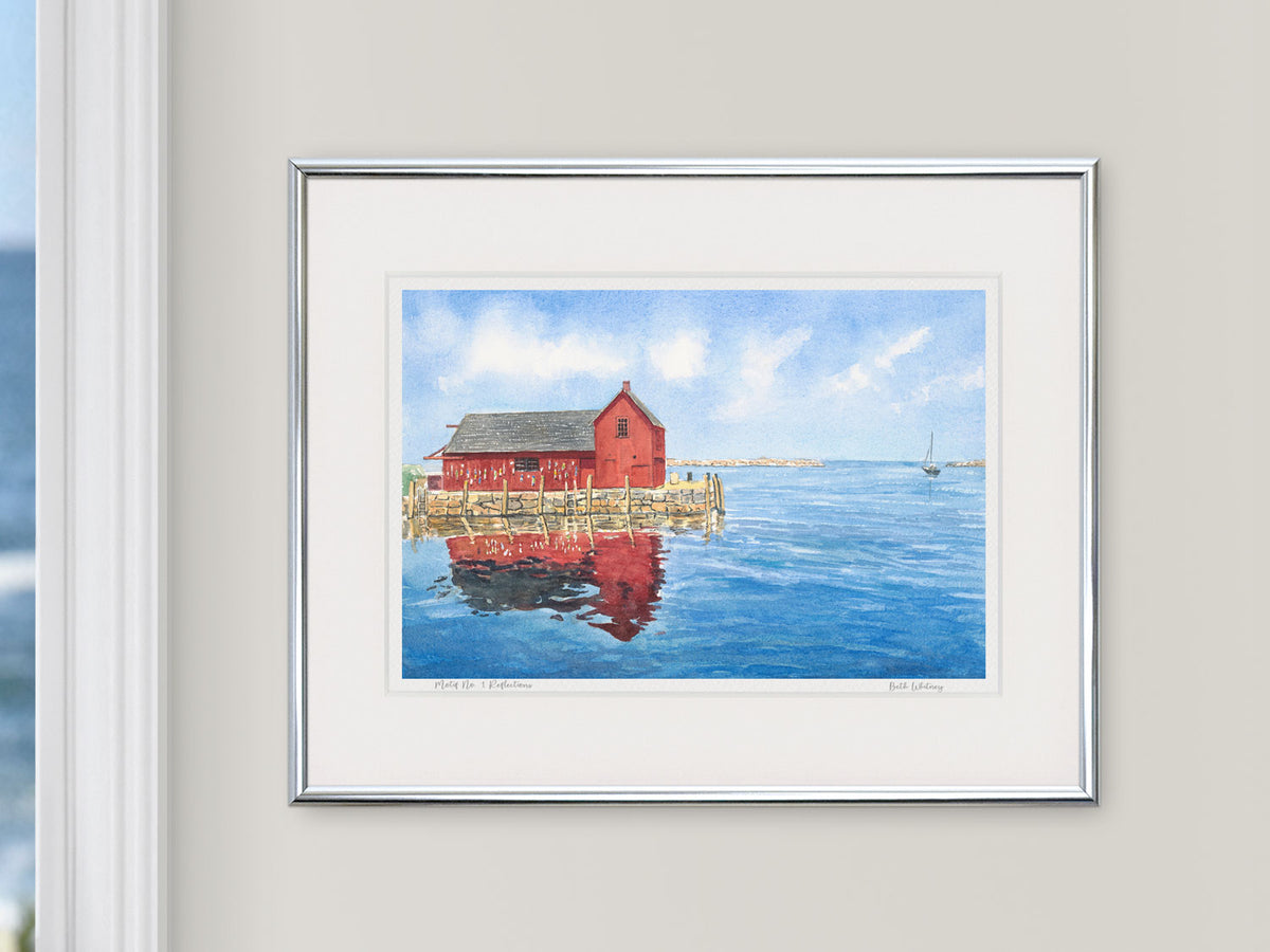 Framed watercolor print of Motif No. 1 Reflections, Bradley Wharf, Rockport, in a silver frame beside a window with an ocean view.