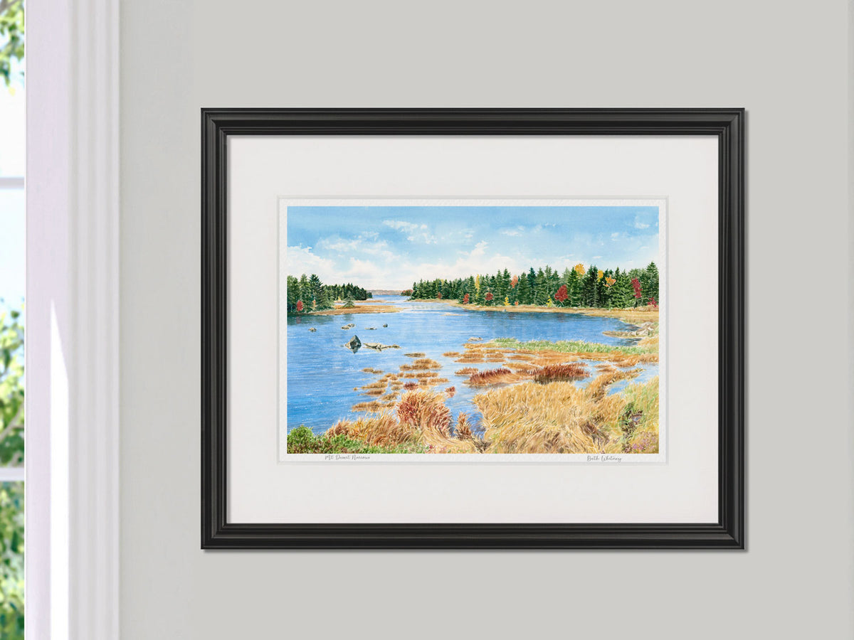 Framed watercolor print of Mt Desert Narrows, Acadia, Maine, in a black frame on a wall beside a window.