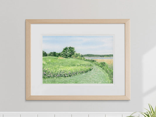 Framed watercolor art print of “North Meadow,” depicting a grassy meadow path at Maine Audubon’s headquarters in Falmouth, Maine, displayed on a neutral wall.