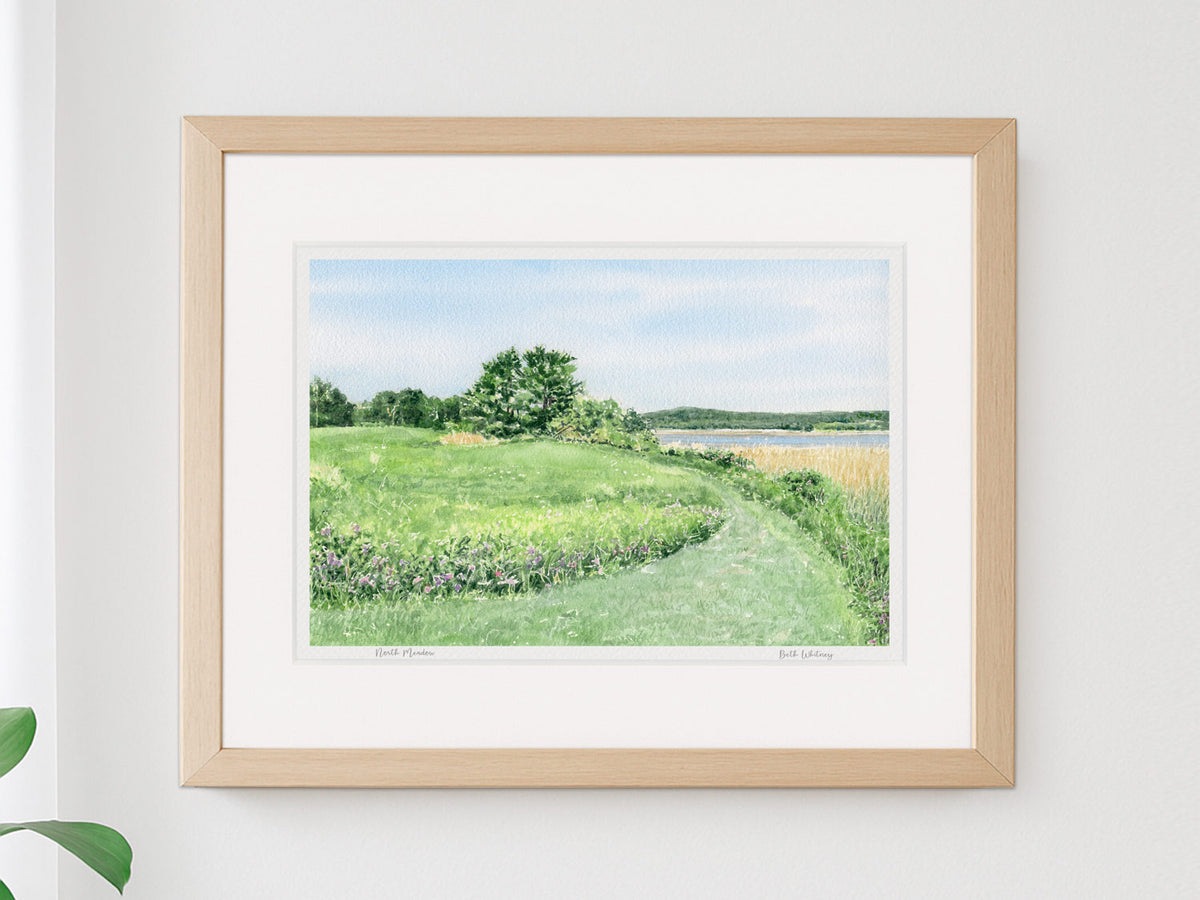 Framed watercolor print of North Meadow, Gilsland Farm, Falmouth, Maine, in a warm wood frame on a neutral wall.
