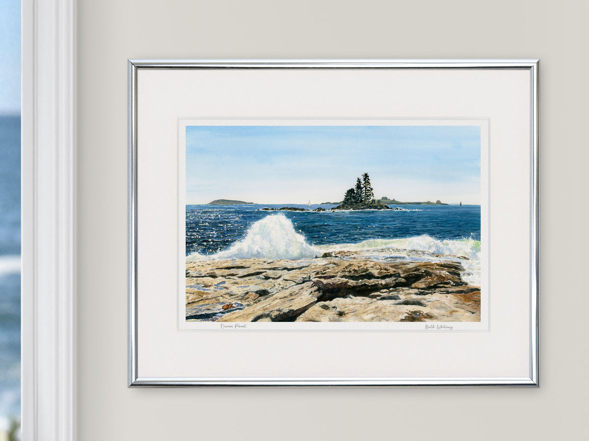 Framed watercolor print of Ocean Point, Boothbay, Maine, in a silver frame on a neutral wall beside a window with an ocean view.