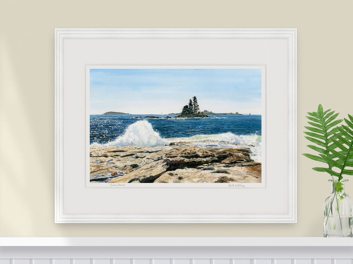 Framed watercolor print of Ocean Point, East Boothbay, in a white frame over a coastal home shelf decor with plant styling.