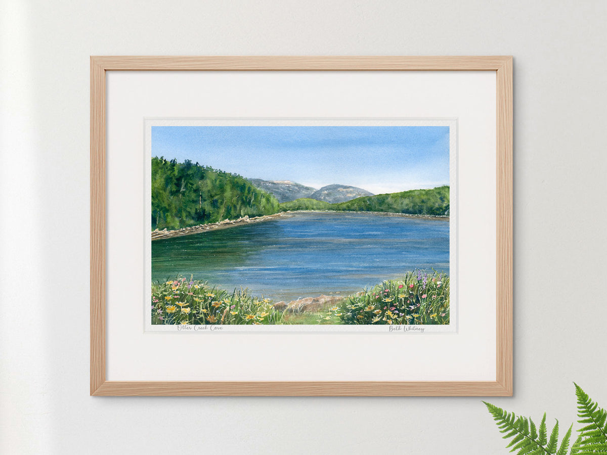 Framed watercolor print of Otter Creek Cove, Acadia National Park, in a warm wood frame on a neutral wall.