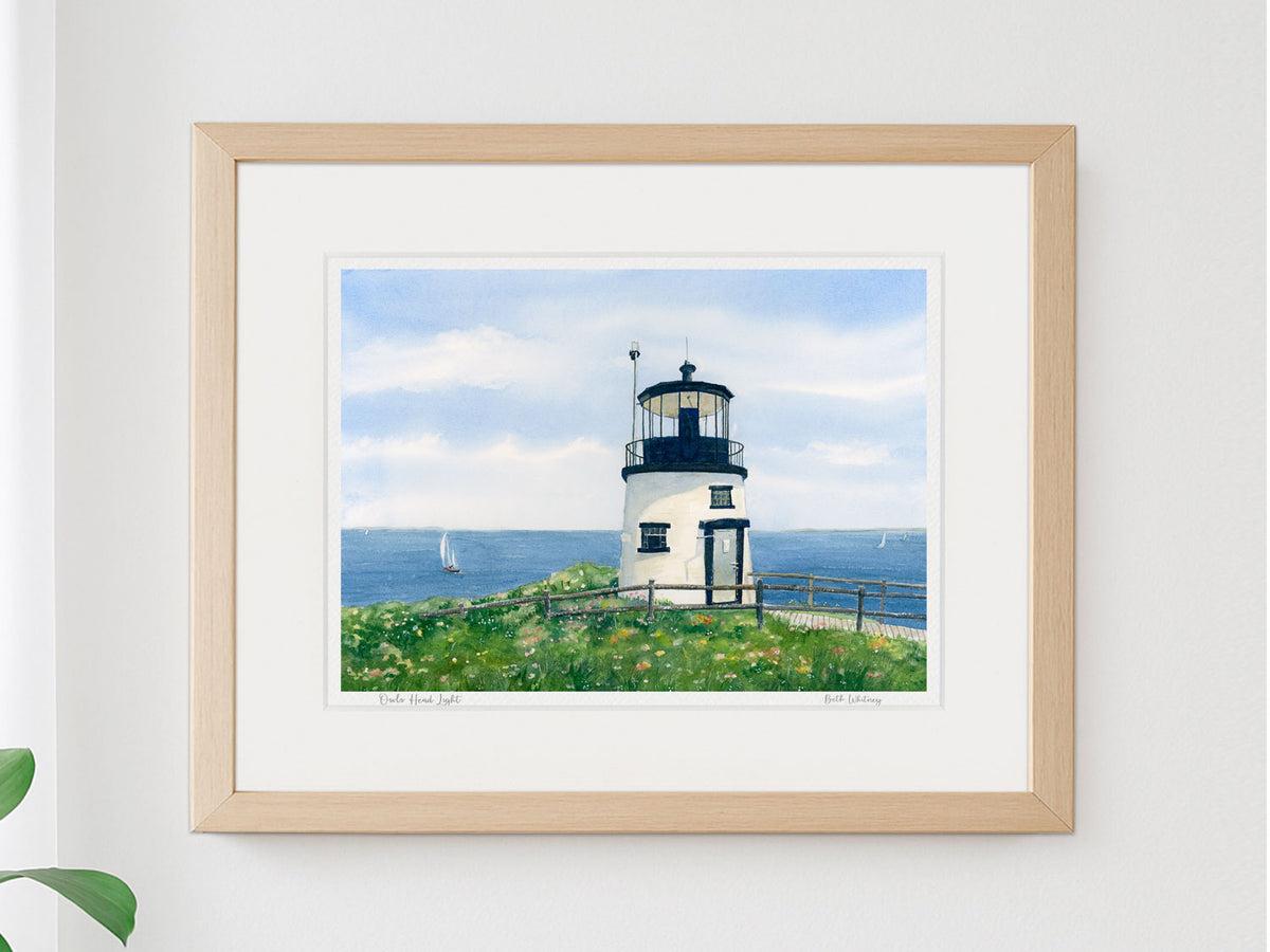 Framed watercolor print of Owls Head Light, Rockland Harbor, Maine, in a warm wood frame on a neutral wall.