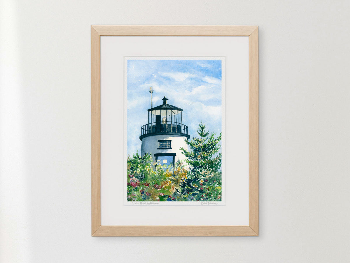 Framed watercolor print of Owls Head Lighthouse, Rockland Harbor, Maine, in a smooth natural wood frame on a wall.