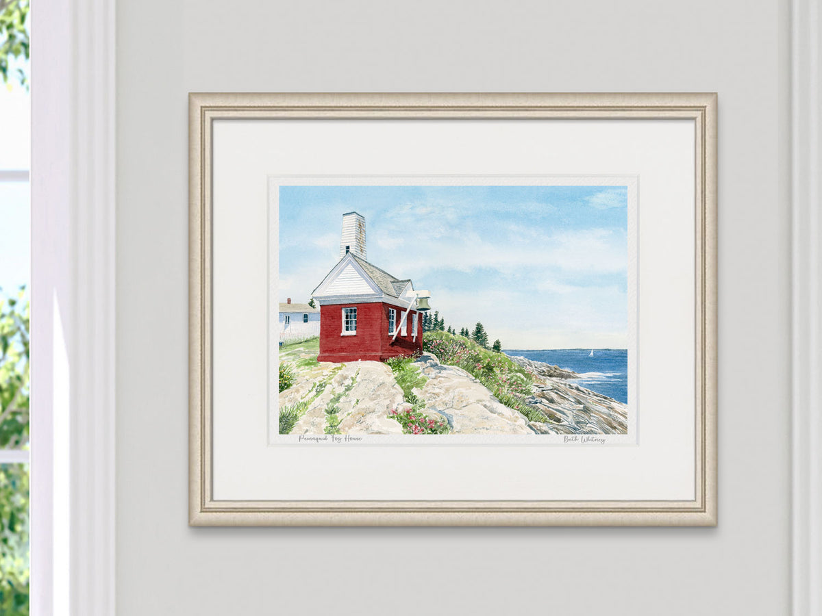 Framed watercolor print of Pemaquid Fog House, Bristol, Maine, in a light gold frame beside a sunny window.