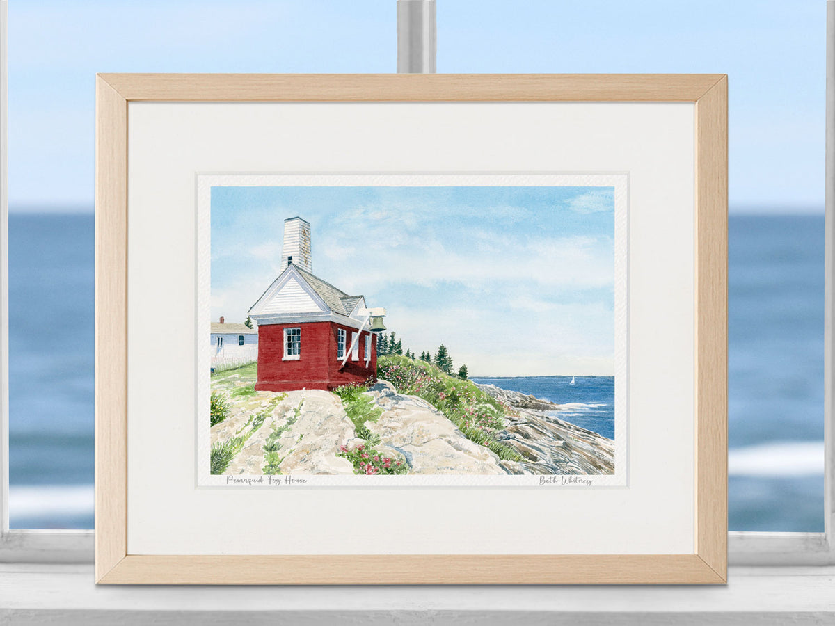 Framed watercolor print of Pemaquid Fog House, Pemaquid Point, in a warm wood frame in a coastal window setting.