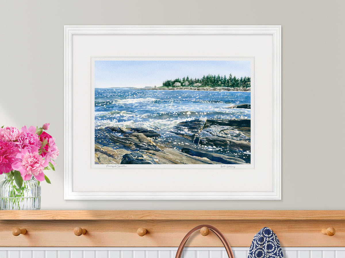 Framed watercolor ocean print of Pemaquid Sparkles, Bristol Maine, in a white frame over a wooden coat shelf with pink peonies.