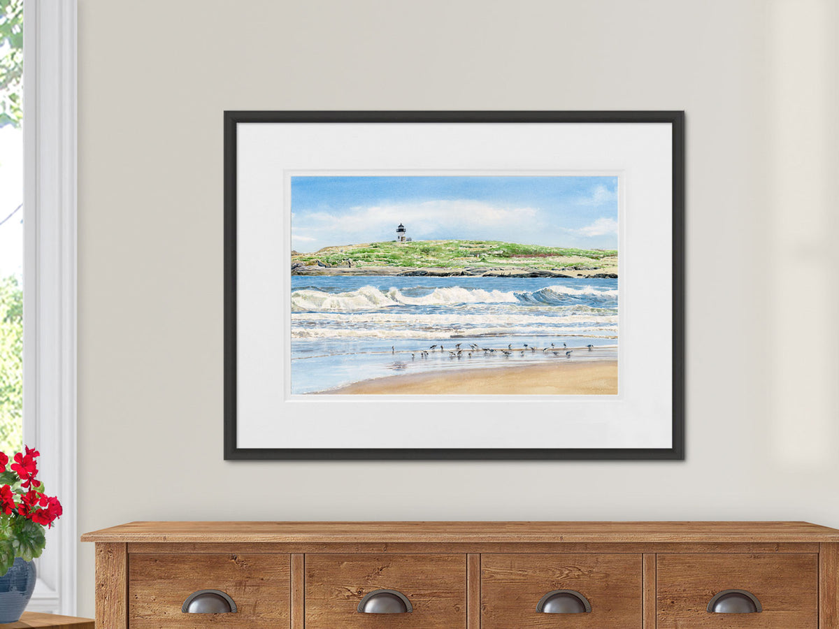 Framed original watercolor painting of Pond Island Light, Popham Beach, Maine, in a black frame on a warm wood dresser.