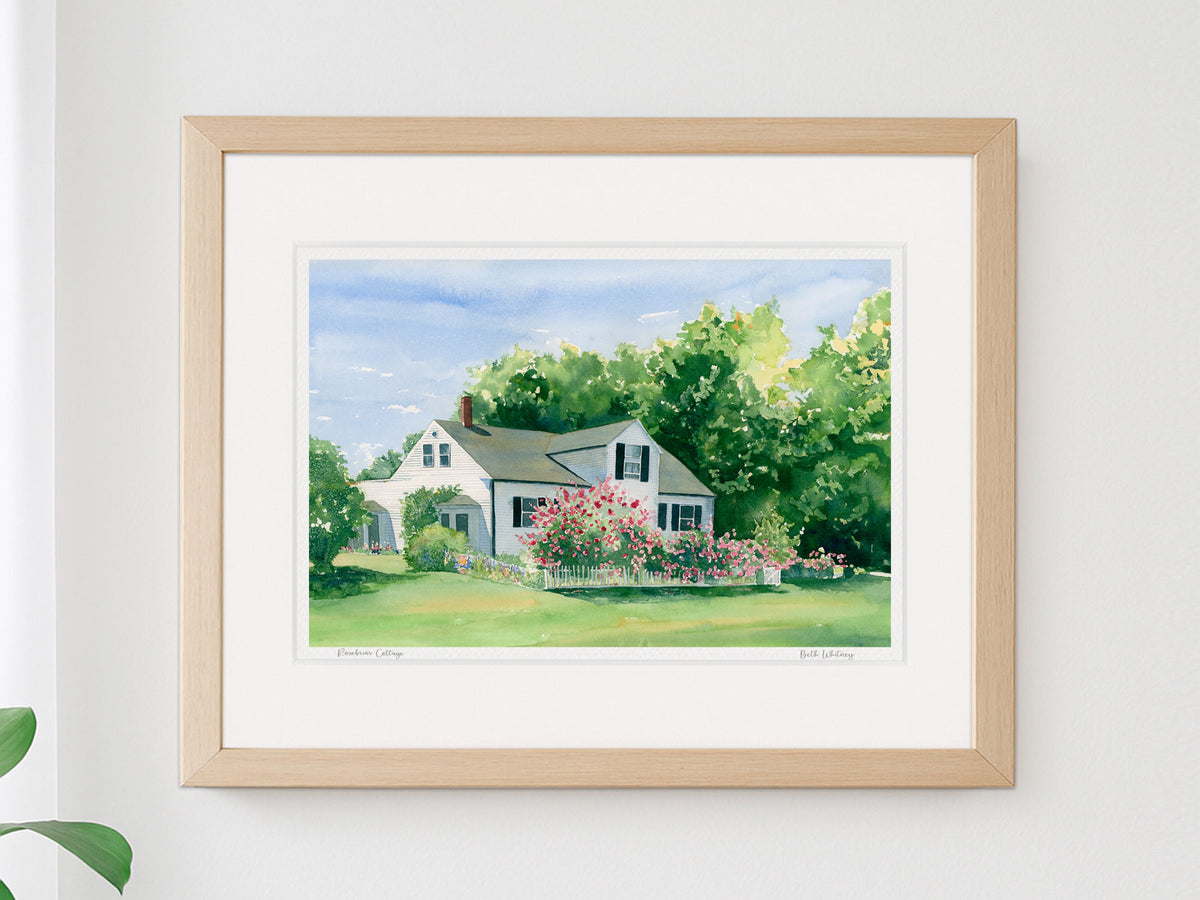 Framed watercolor print of Rosebriar Cottage, a Maine cottage and rose garden, displayed in a warm wood frame on a neutral wall.