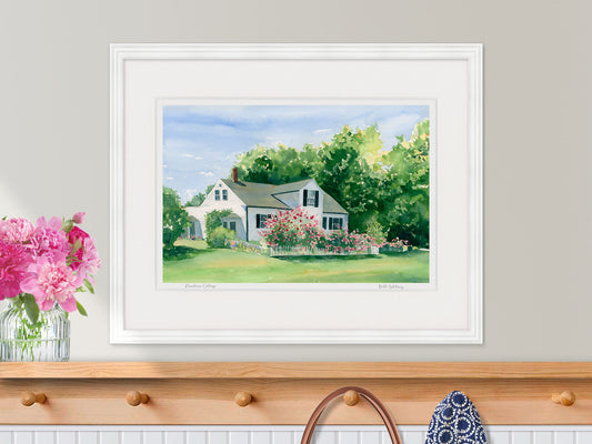 Framed watercolor print of Rosebriar Cottage, a pink rose garden in Blue Hill, Maine, displayed in a white frame with fresh peonies over a coastal style entryway shelf.