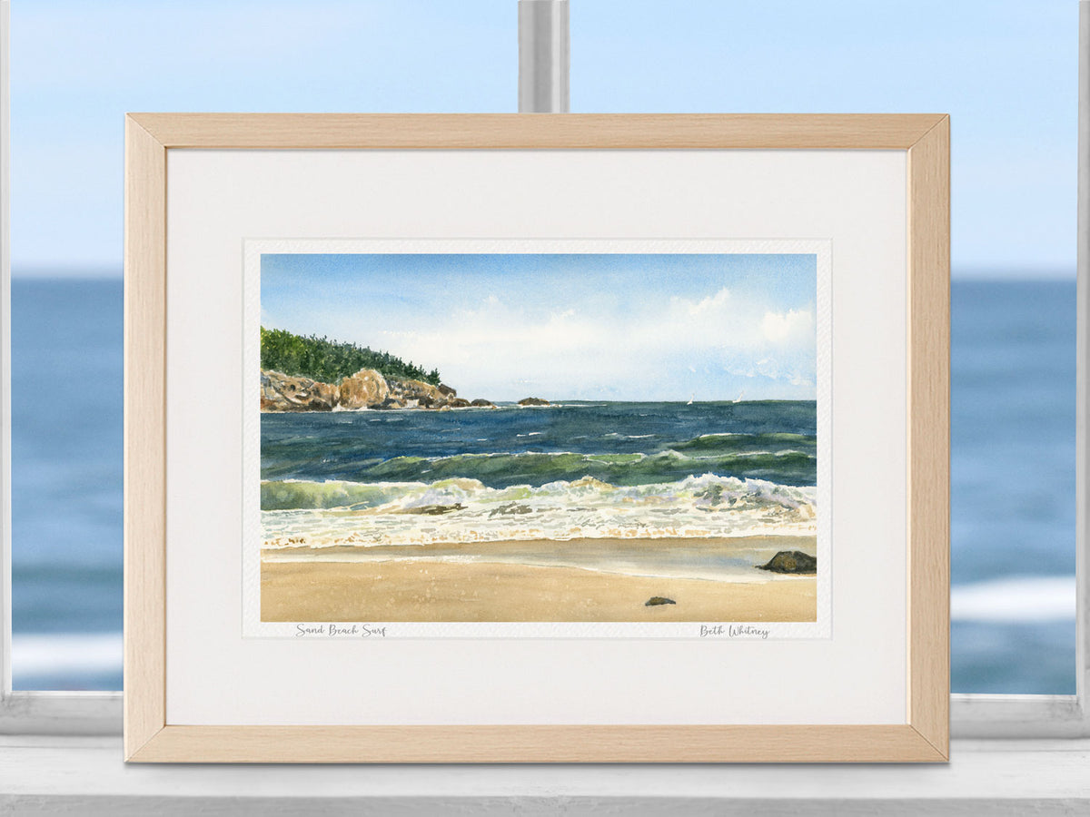 Framed watercolor print of Sand Beach Surf, Sand Beach, Acadia, in a warm wood frame in a coastal window setting.