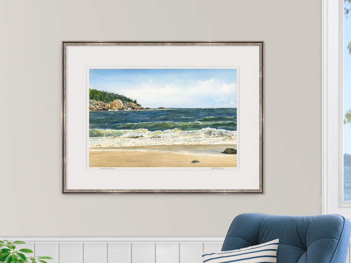 Framed watercolor print of Sand Beach Surf, Acadia National Park, Maine, in a gold frame with blue chair in a nautical lifestyle setting.