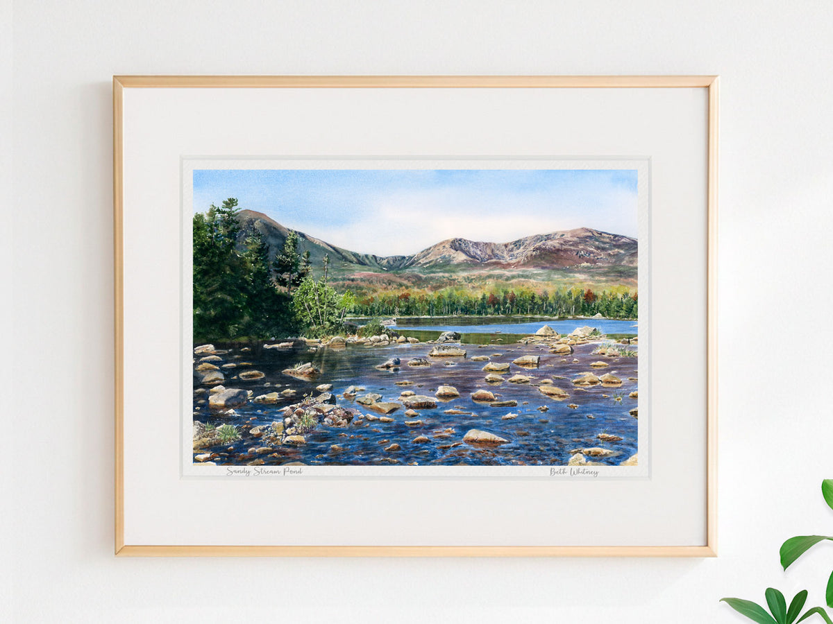 Framed watercolor print of Sandy Stream Pond, Baxter State Park, Maine, in a simple gold frame on a sunny wall.