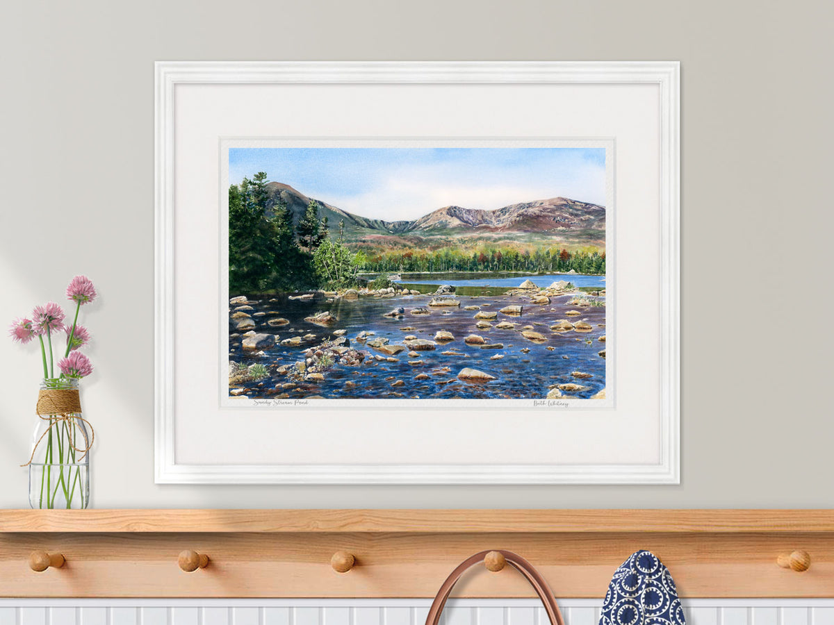 Framed watercolor print of Sandy Stream Pond, Baxter State Park, in a white frame with flower styling over an entryway decor.