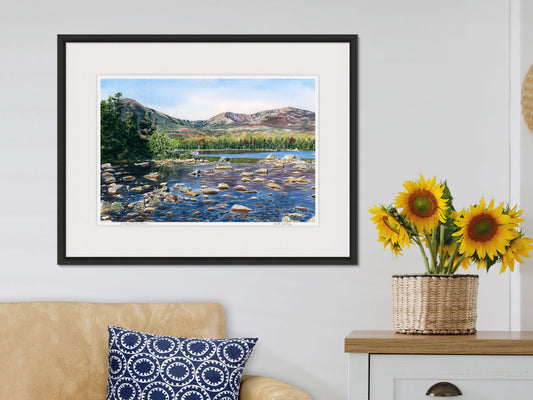 Framed watercolor print of Sandy Stream Pond, Mt Katahdin, Maine, in a black frame over a tan sofa with sunflower styling.