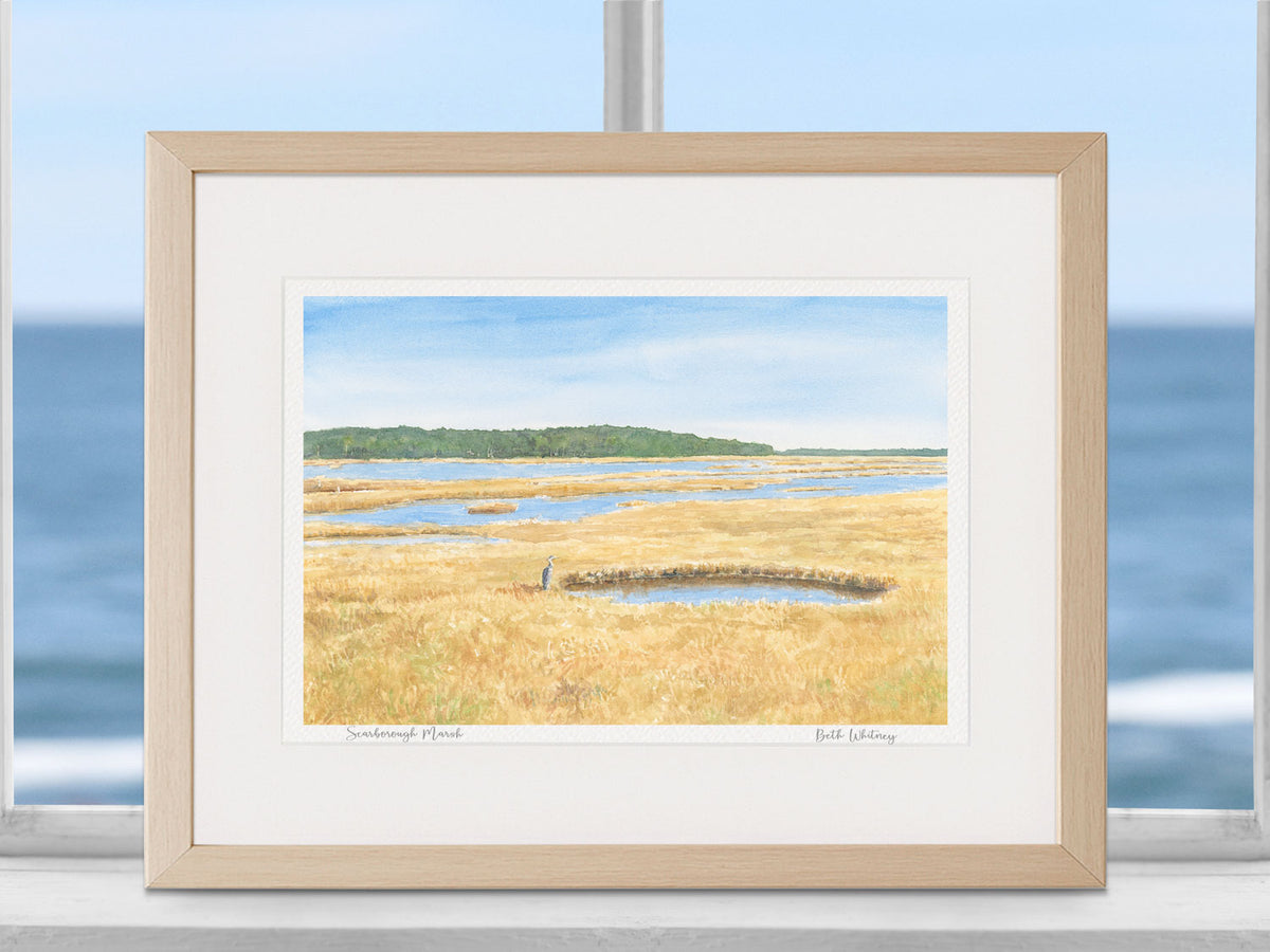 Framed watercolor print of Scarborough Marsh, Maine, in a warm wood frame on a coastal window sill decor.