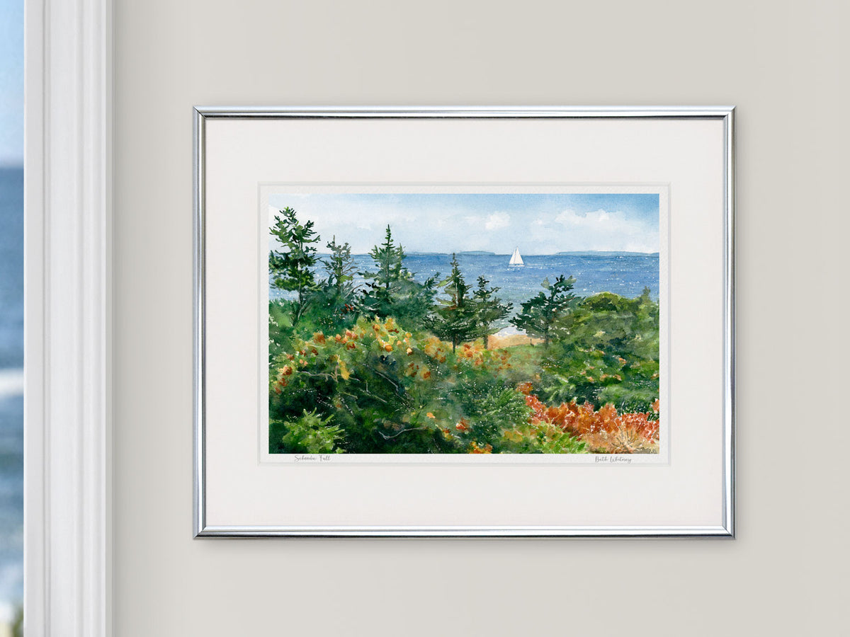Framed watercolor print of Schoodic Fall, Frenchman's Bay, Maine, in a silver frame beside a window with an ocean view.