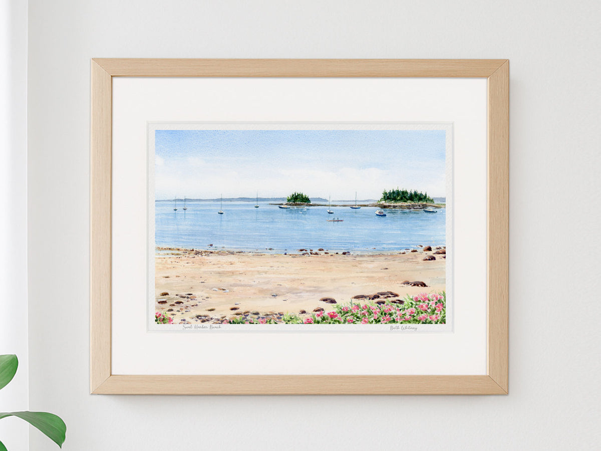 Framed watercolor print of Seal Harbor Beach, Acadia, Maine, in a warm wood frame on a neutral wall.