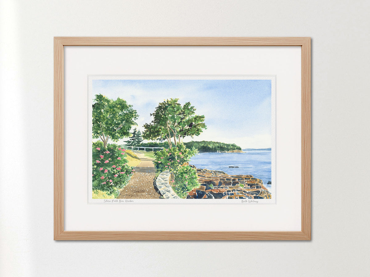 Framed watercolor print of Shore Path Bar Harbor, Maine, in a warm wood frame on a neutral wall.